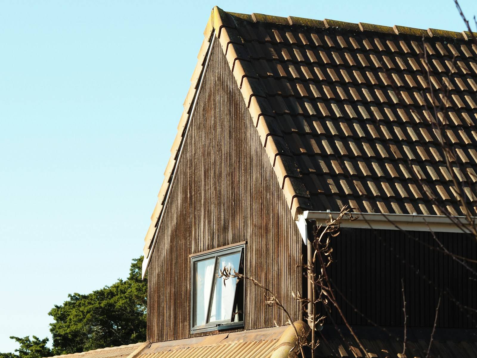 Woning met donker verweerde houten gevelbekleding en een dak met pannen